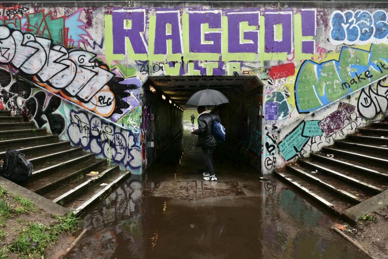 A man holding an umbrella walks through a flooded underpass entrance at Lawrence Hill roundabout