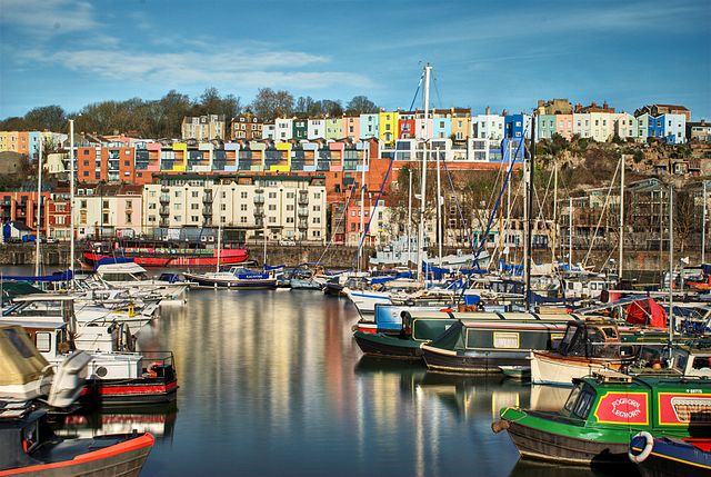 Bristol Marina in the sunshine, with a number of boats and colourful terraced houses on the hill