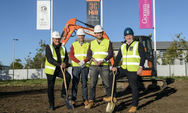 Men in hard hats and hi-vis jackets pose in front of a Goram Homes building site.
