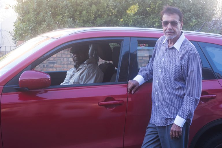 Adult man in shirt standing by car occupied by driver at the wheel.