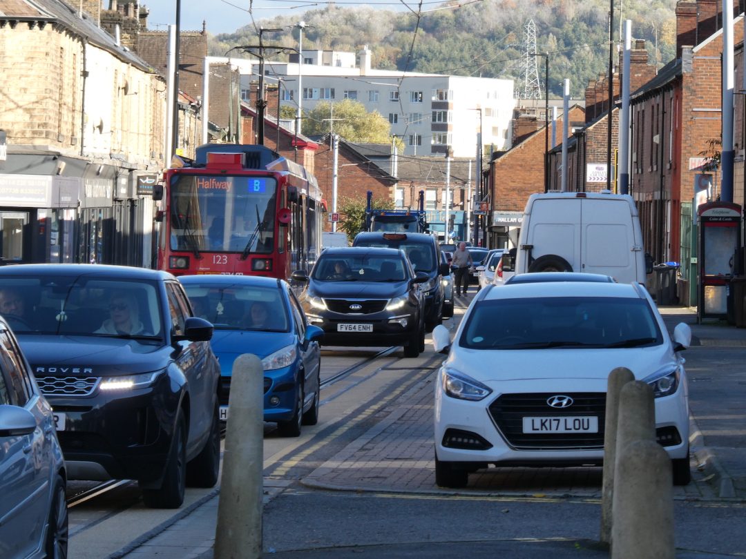 A busy street with a tramline and a queue of cars.