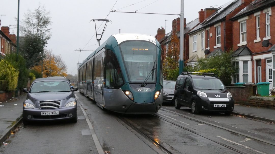 A tram running down the middle of a residential street with cars parked opposite.