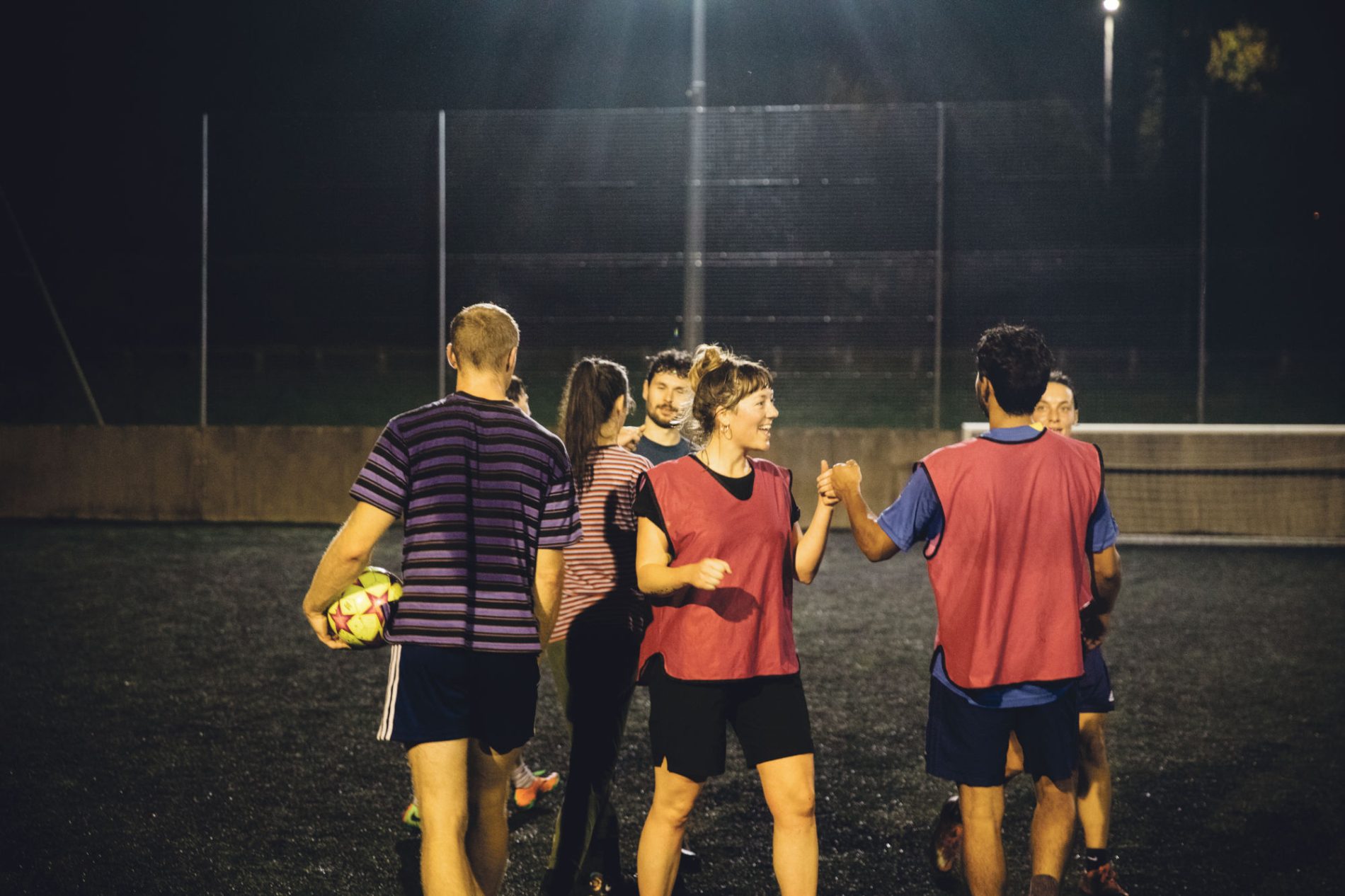 A group of mixed gender football players exchange fist bumps at the end of match on an autumnal evening.