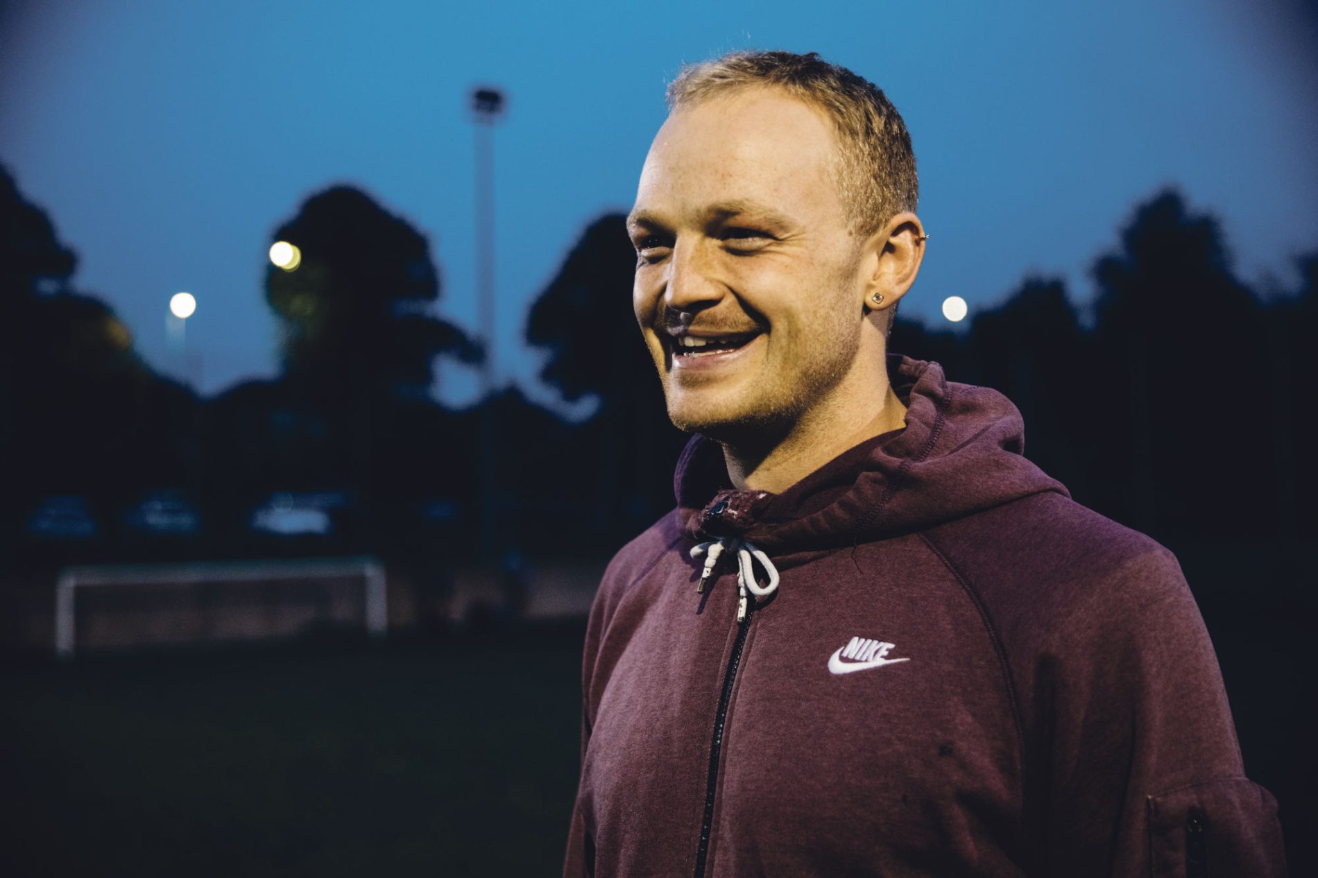 A man wearing a hoodie has a beaming smile while playing football under the floodlights. 