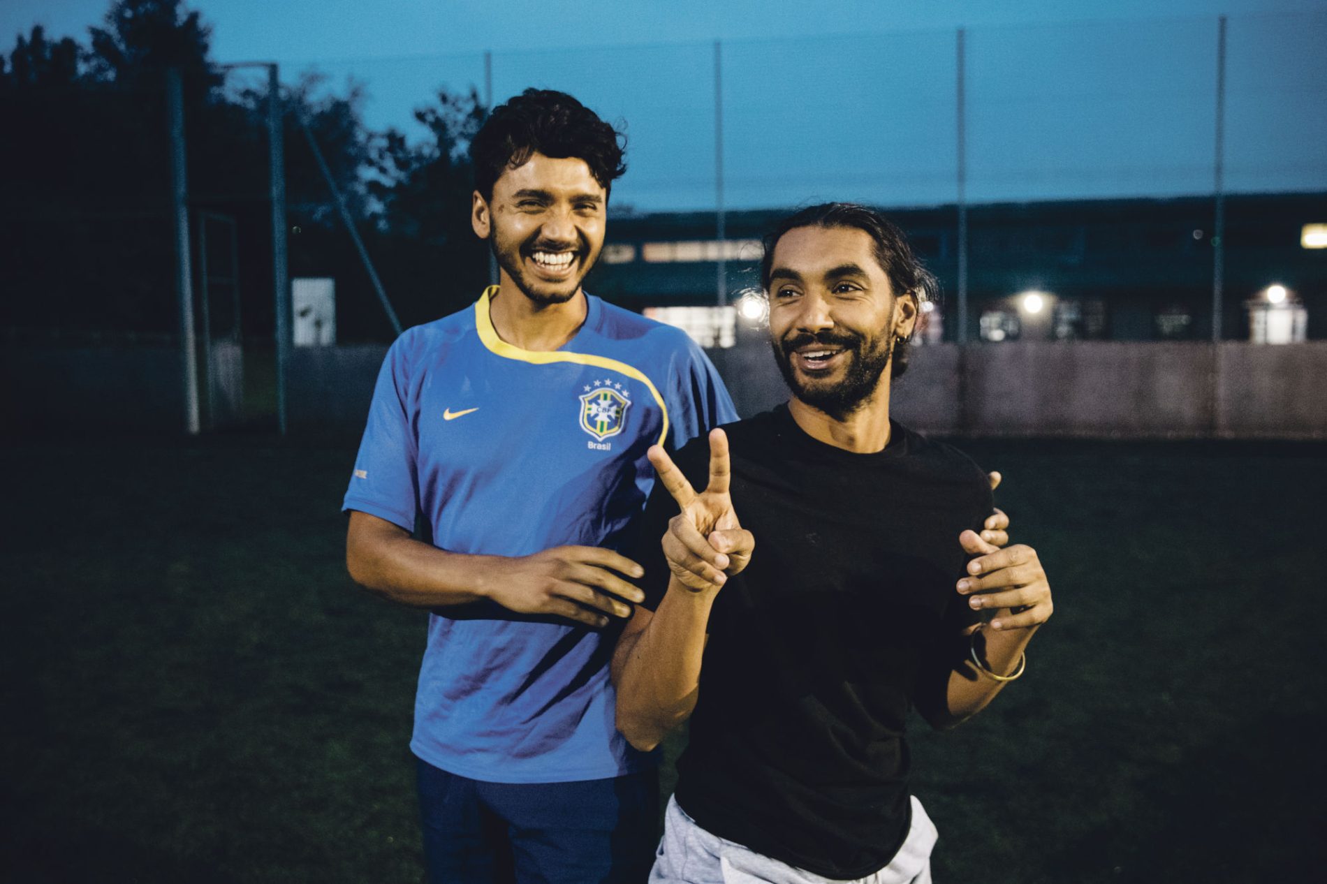 Two men joyfully celebrate together after playing a football match. One of them is making a peace sign. 