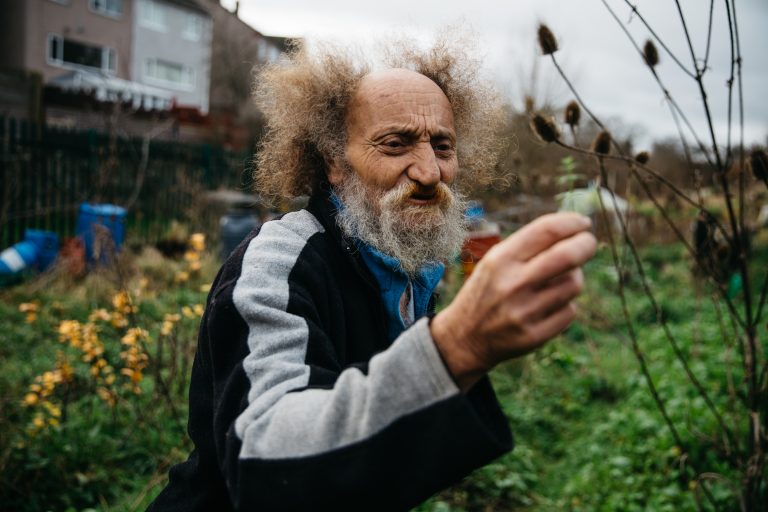 A bearded man holds a small green shoot on an allotment site