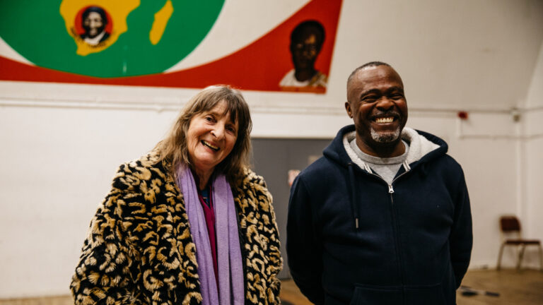 A woman and a man stand smiling in the hall of a community centre