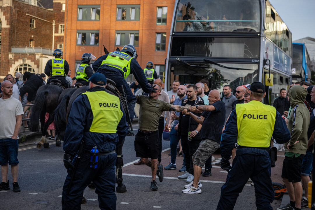 A police officer on horseback pushes back a far right protester by putting his hand in his face, while other protesters on Bristol Bridge look on