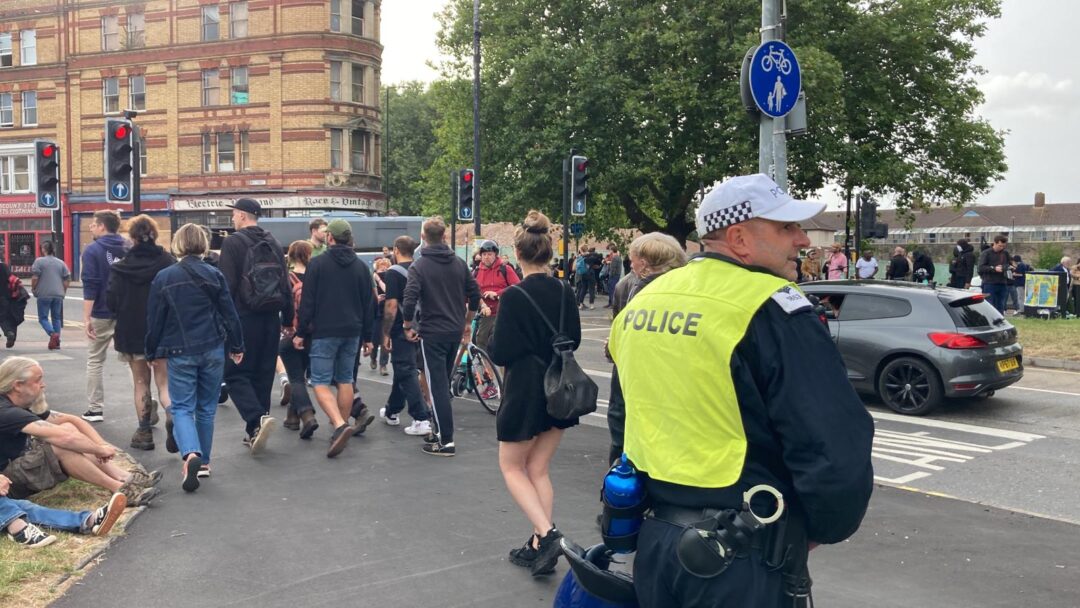 A police officer and group of protesters stand on a street corner by Old Market in Bristol