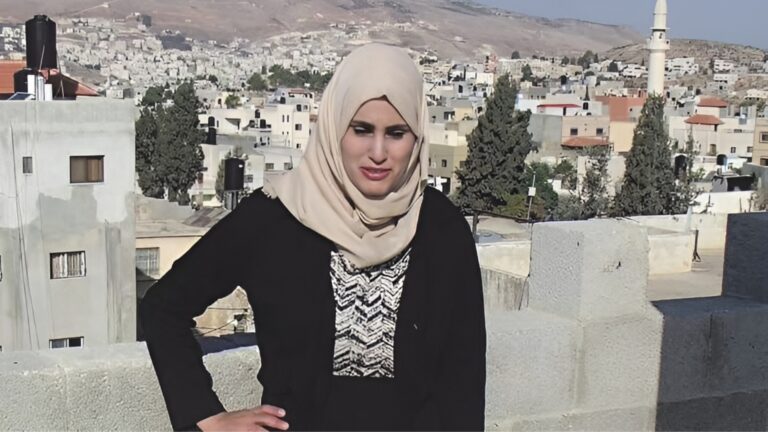 A palestinian teacher in a headscarf standing outside.