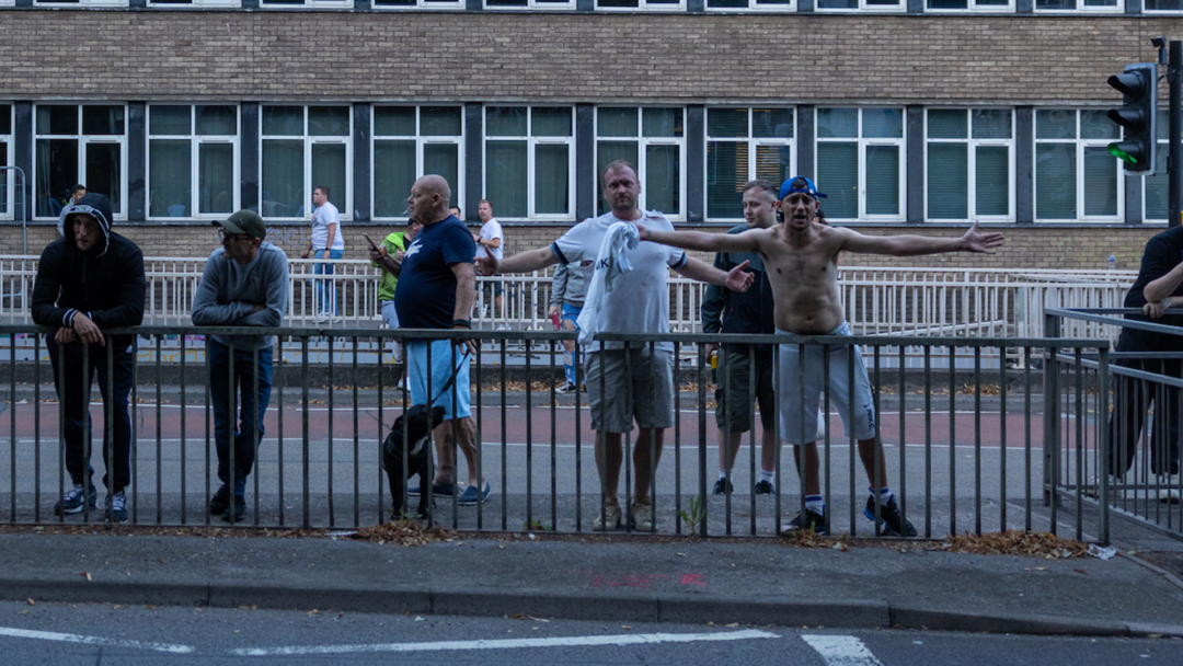 A group of people stand opposite a railing on a roadside.