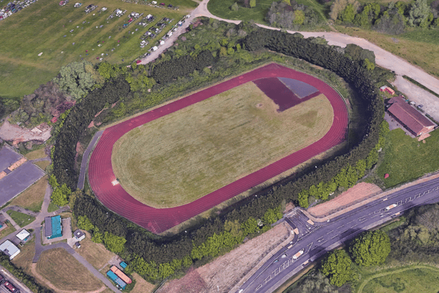 Overhead perspective of an athletics track, highlighting the vibrant green turf and red running track. 