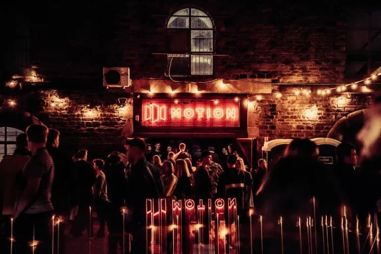 A nightclub entrance with red neon lighting and people waiting outside.
