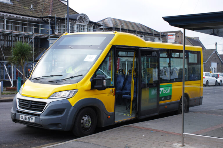 A bright yellow bus parked on the street with its door open. A building with scaffolding is in the background