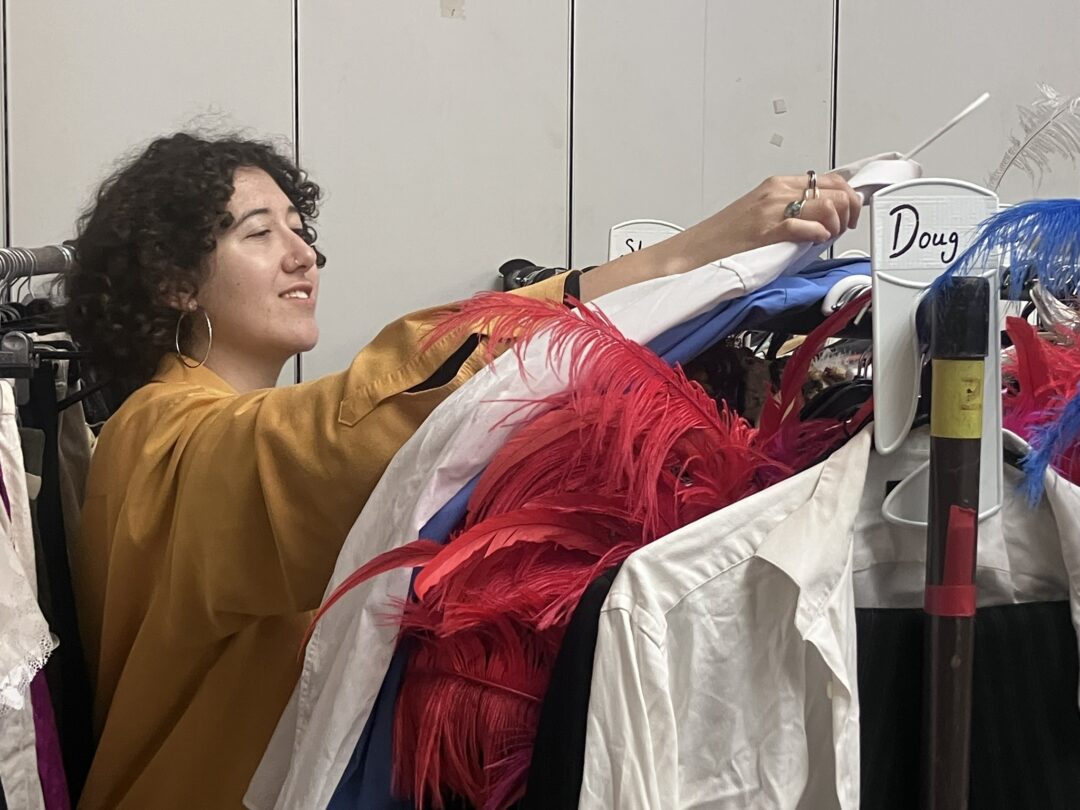 A woman in a bright yellow jacket and large hoop hearings searches for clothes on a clothes rack