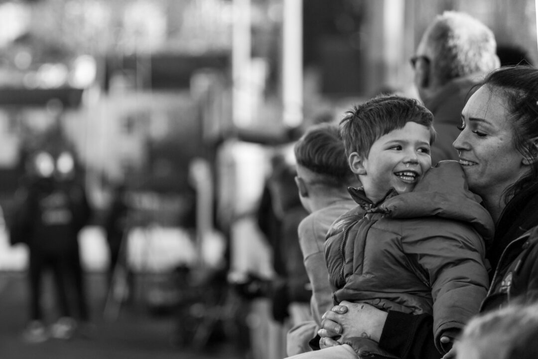 A woman holds a young boy, both smiling as they stand on a football terrace.