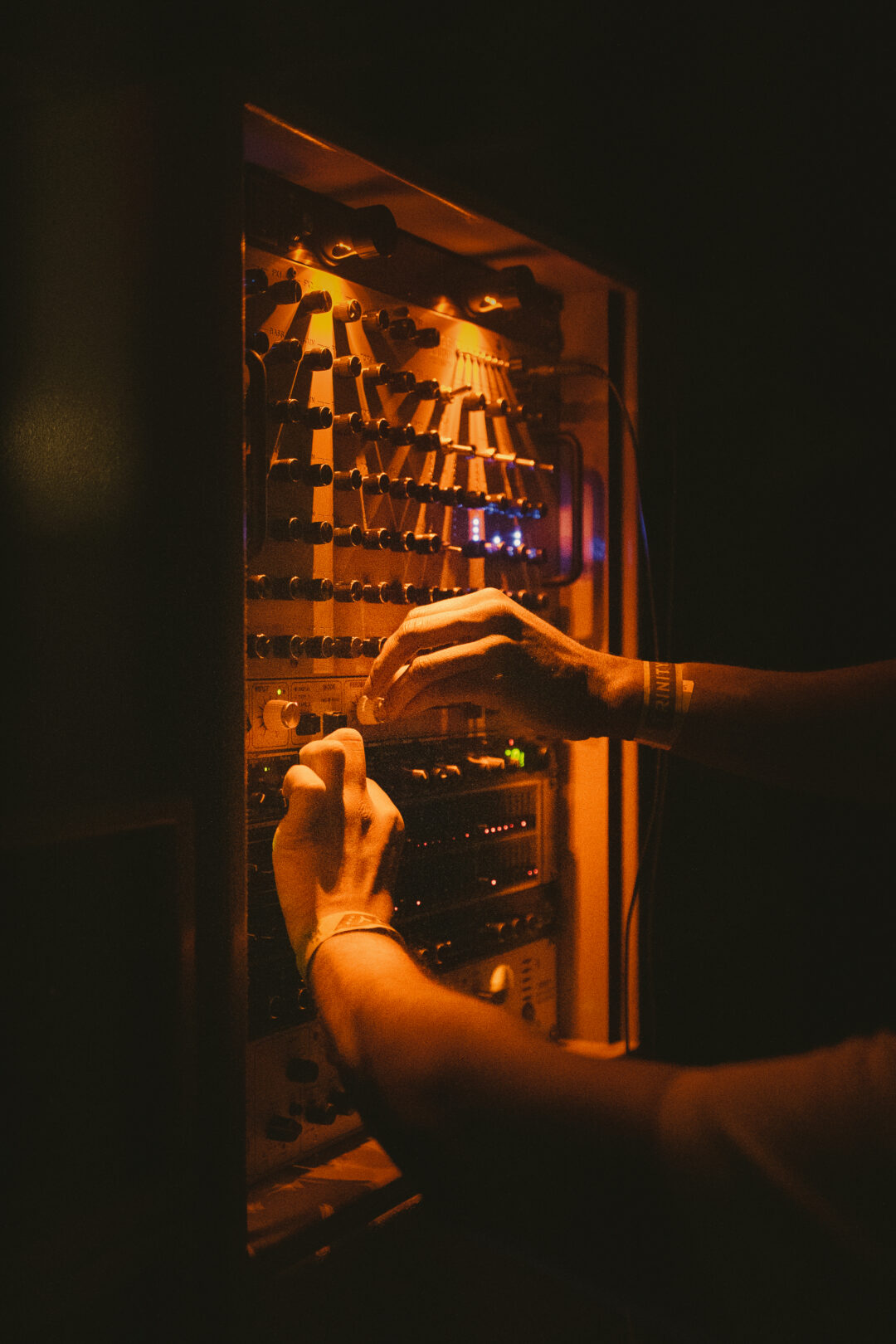 Two hands turning knobs on an audio mixer in a dark room.