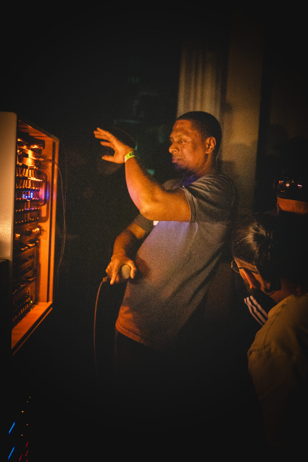 A man holding a micrphone dances in a front of an audio mixer in a dark room.