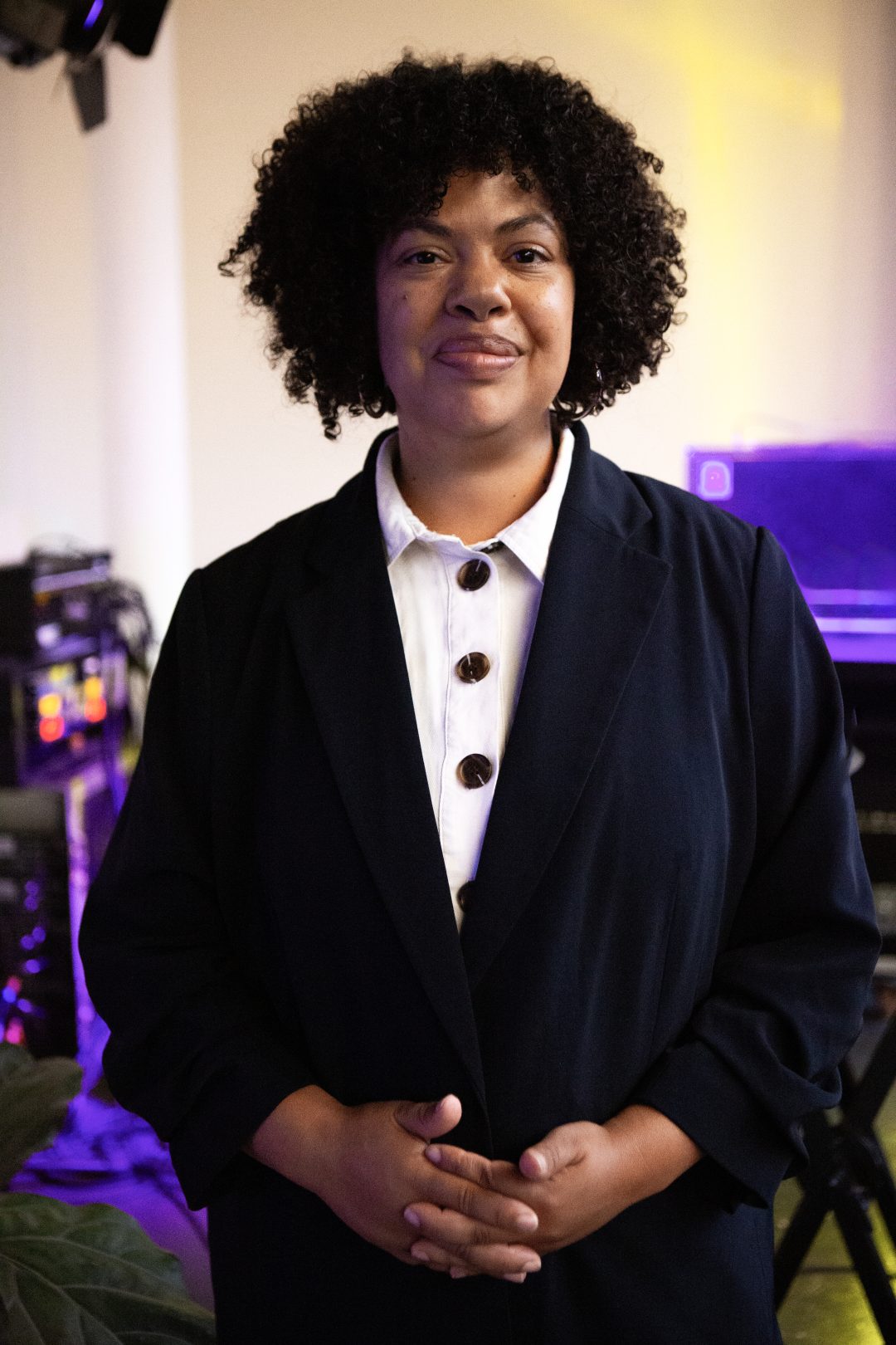A woman stands wearing a dark blue jacket and white shirt. 