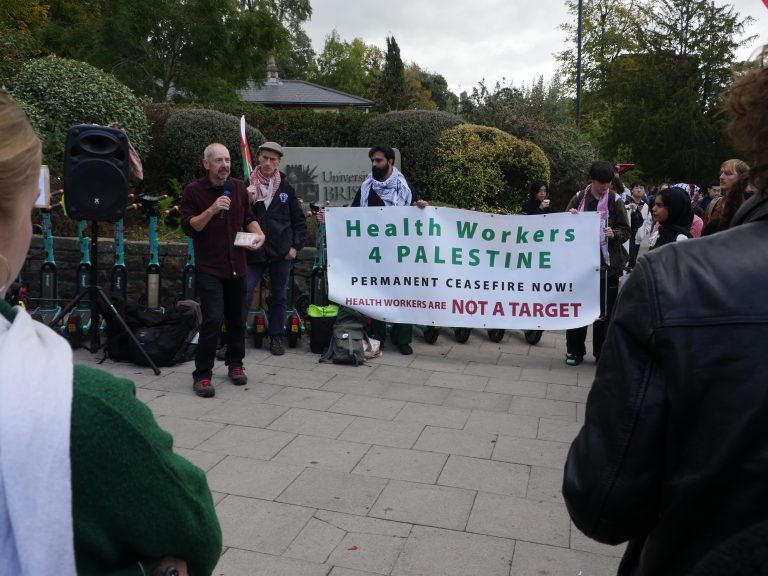 A group of people stand on the pavement beside a white banner.