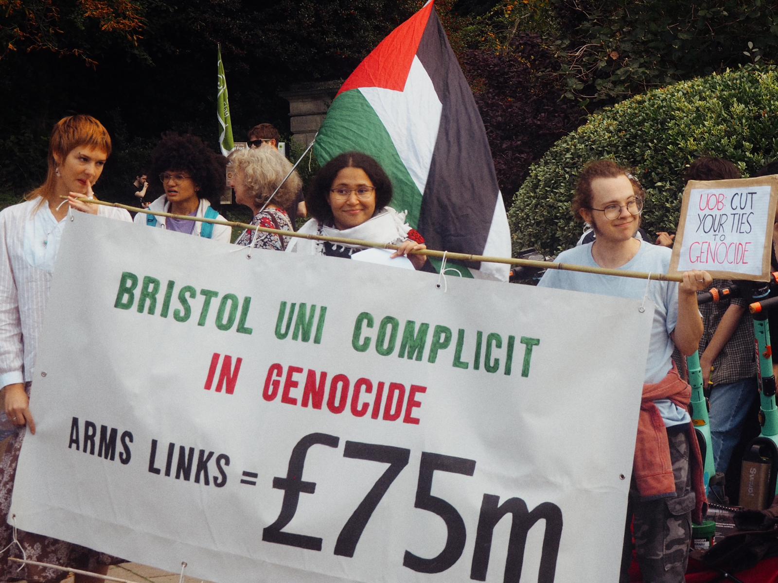 Three students hold a large white banner at a protest.