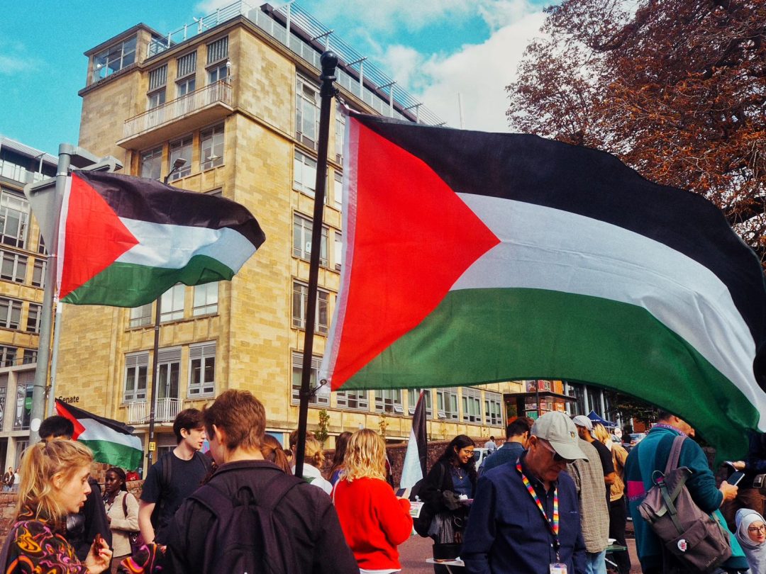 A group of people on the street standing next to large Palestinian flags. 