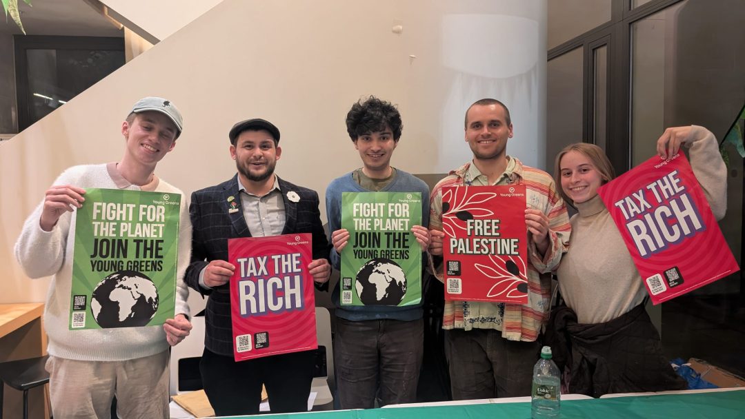 A group of five people stand holding green and red placards. 
