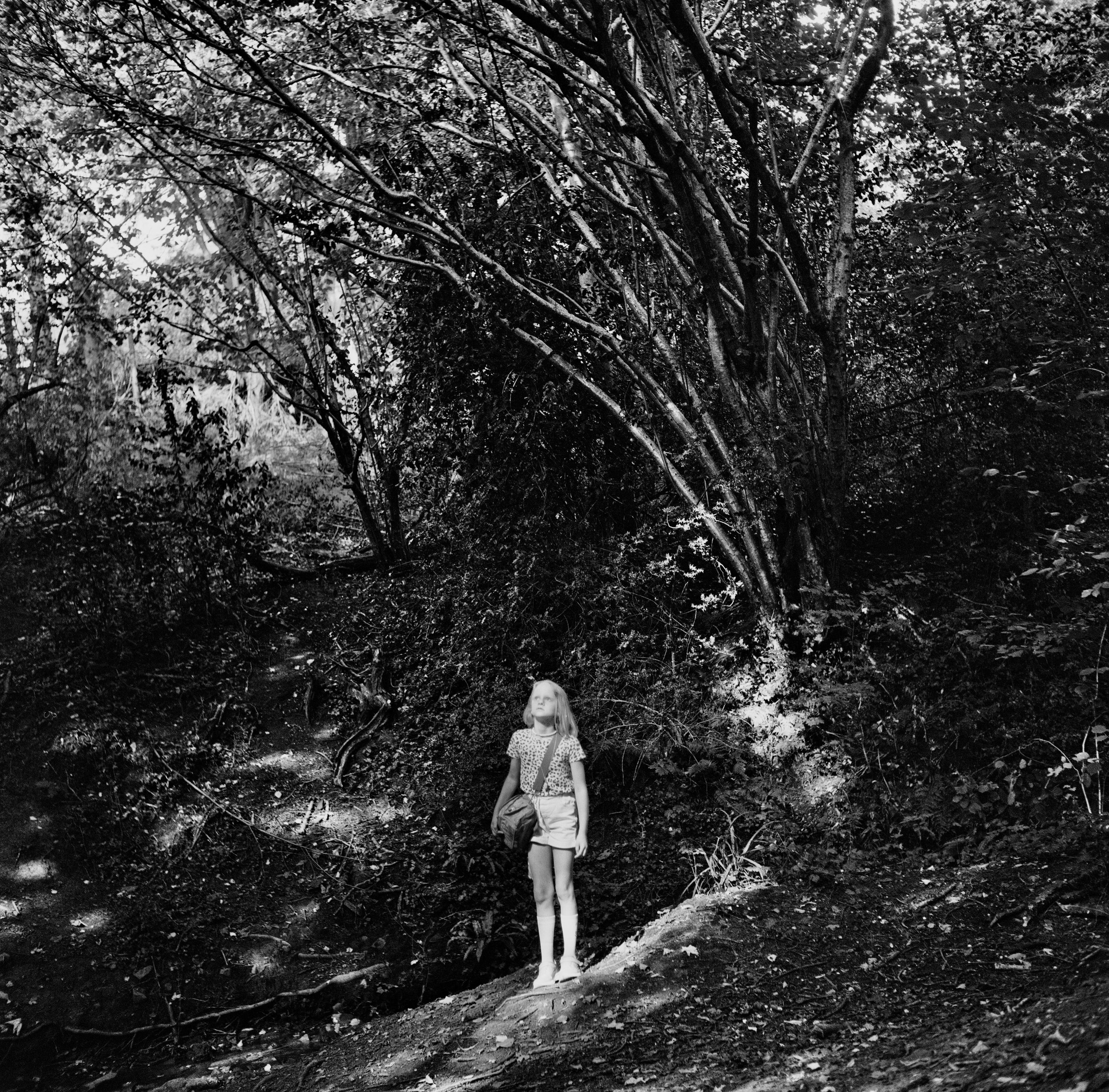 A girl stands on a slope and looks up, surrounded by nature.