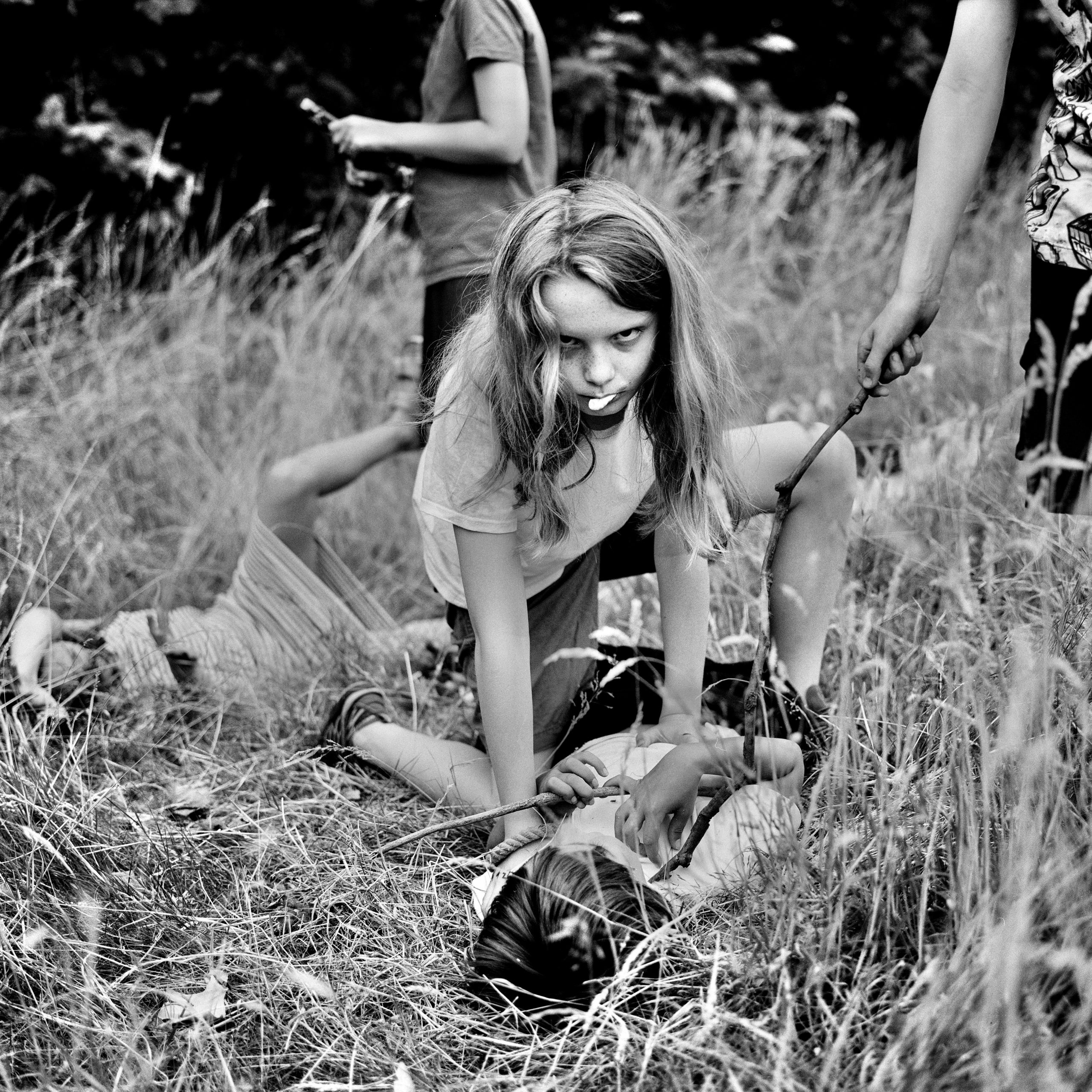 A girl kneels over a boy, among a group of other children playing a park.