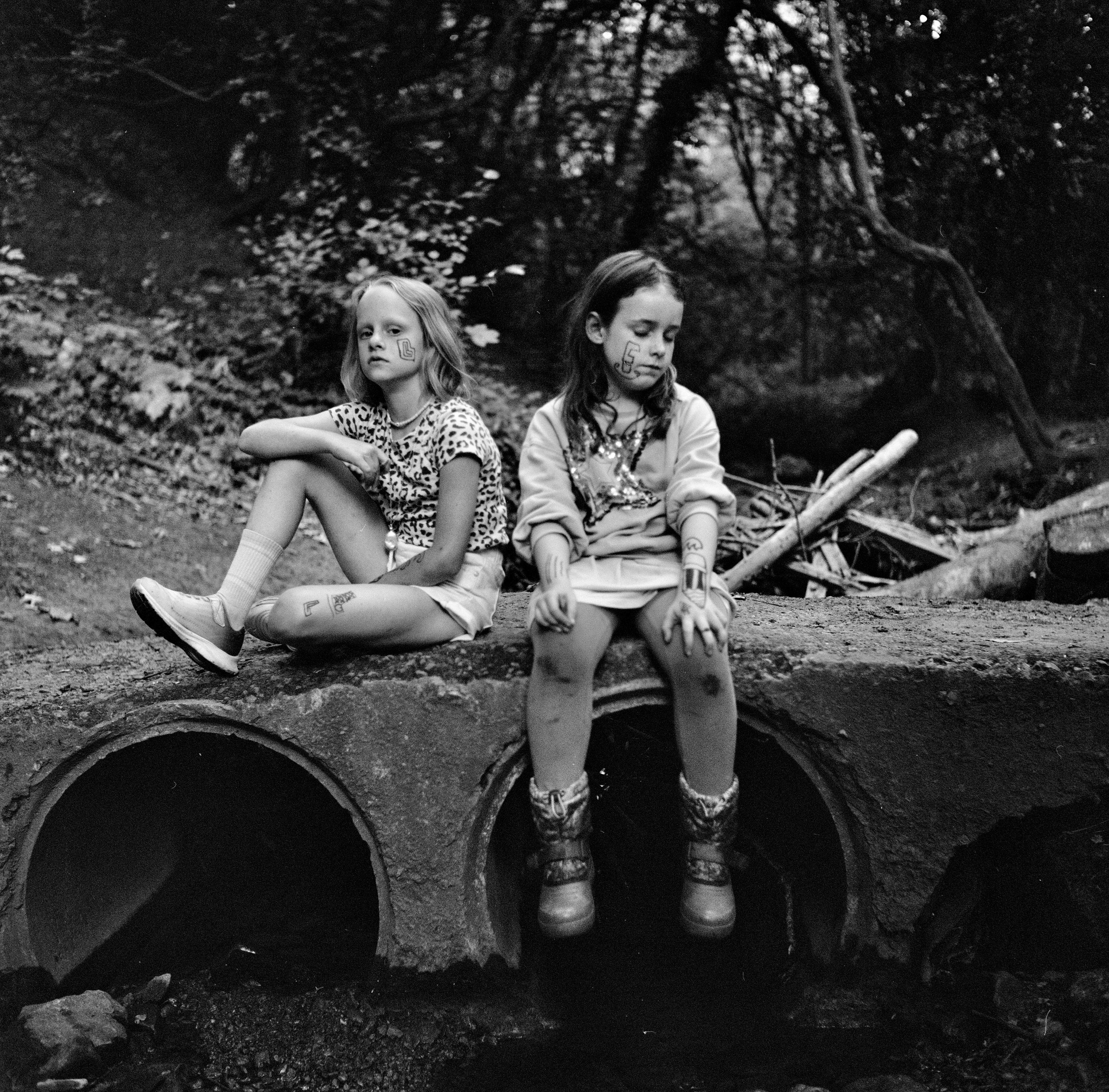 Two girls sit above a water pipe in a park.