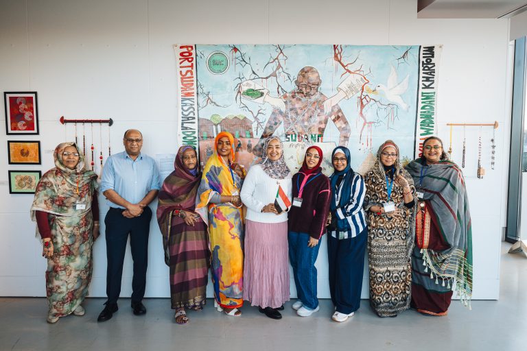 A group of women and one man in colourful clothes standing in front of a mural