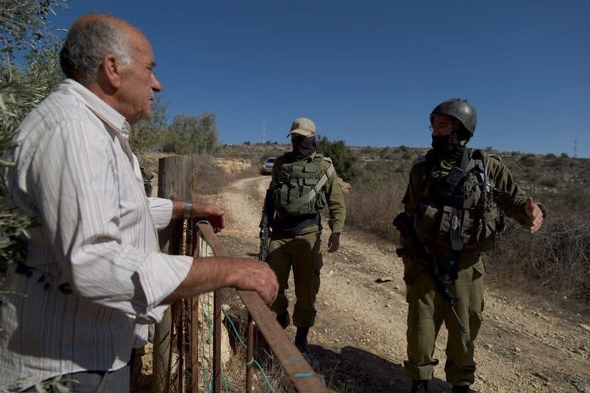 A farmer stands behind a fence looking at two soliders