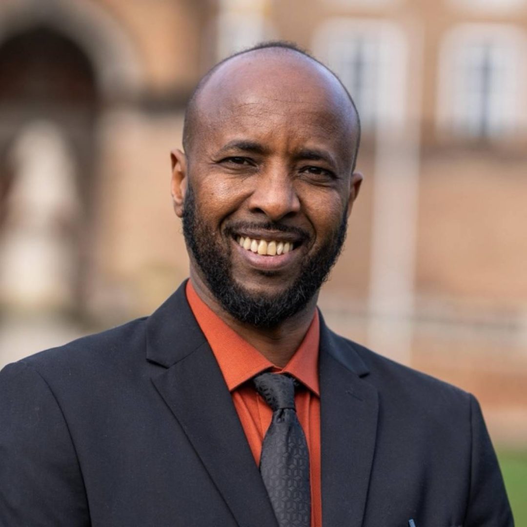 A man in a dark suit and and orange shirt smiling
