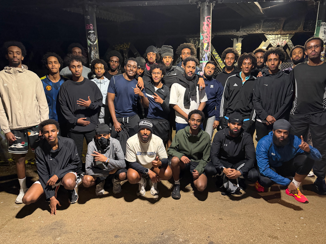 A group of young men in tracksuits prepare for a run, next to the pillars of a bridge qhxidiqxkiqtzinv
