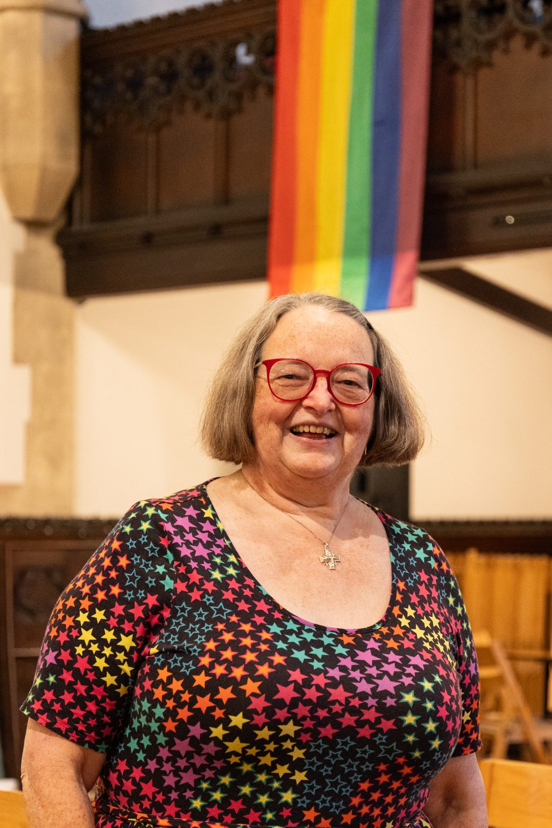 A woman in a colourful top smiles in front of a rainbow flag
