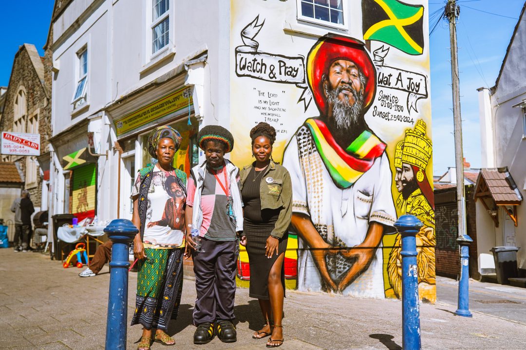 Three people standing next to a colourful mural on a street corner