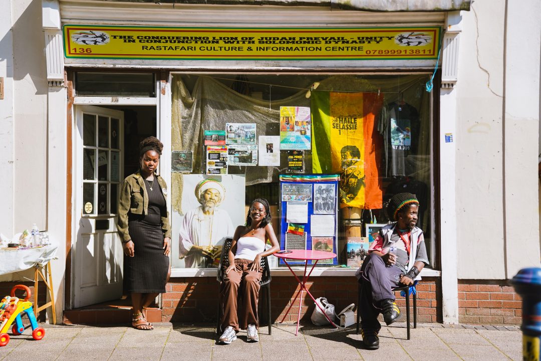 Three people outside a shop front covered in posters, flags and photographs