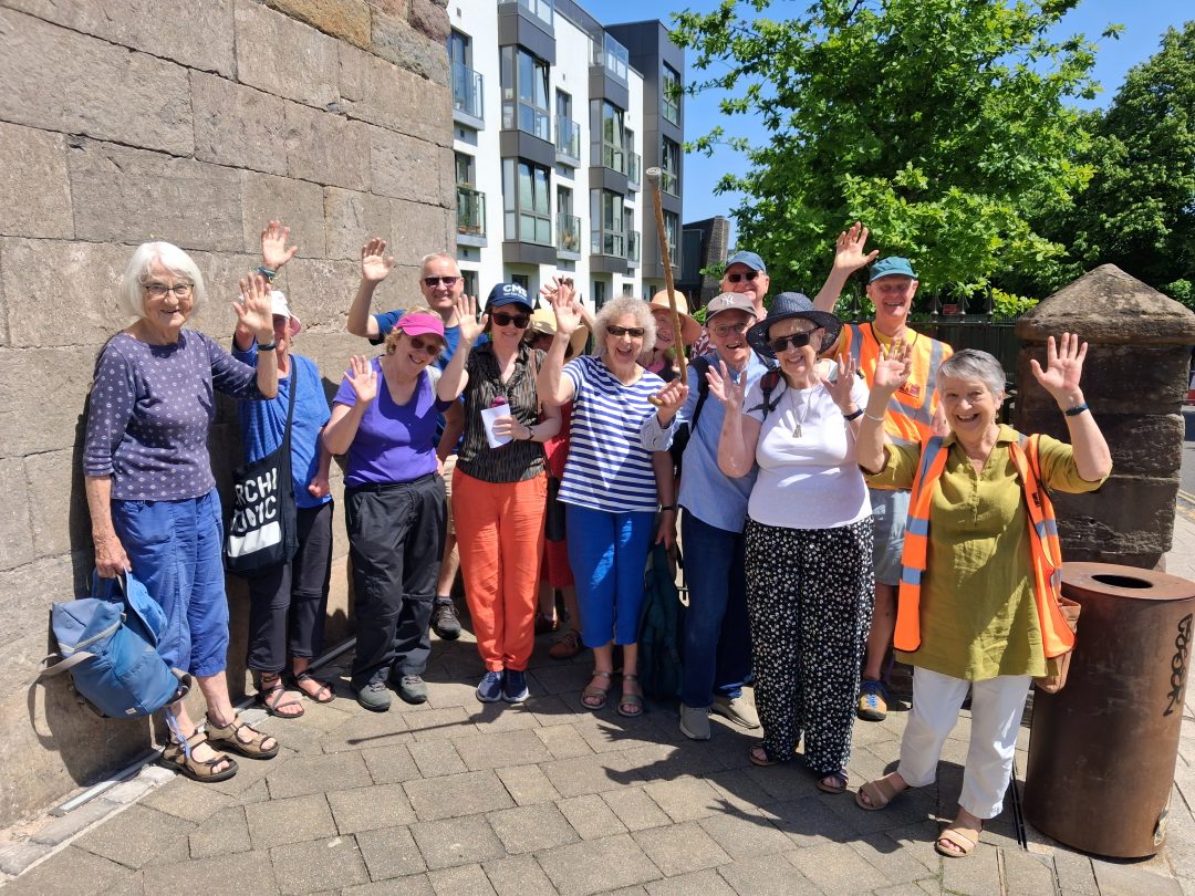 A group of older people smiling and waving next to a concrete wall