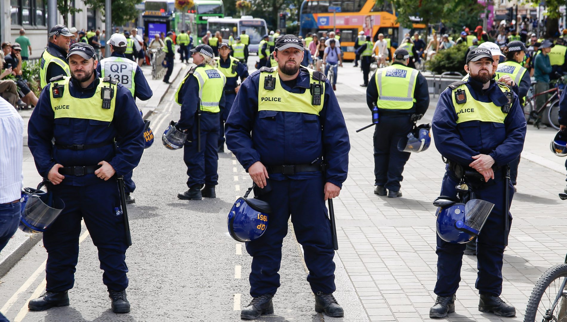 A line of police officers wearing high-visibility jackets and carrying riot helmets
