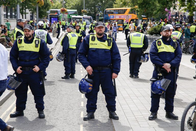 A line of police officers wearing high-visibility jackets and carrying riot helmets